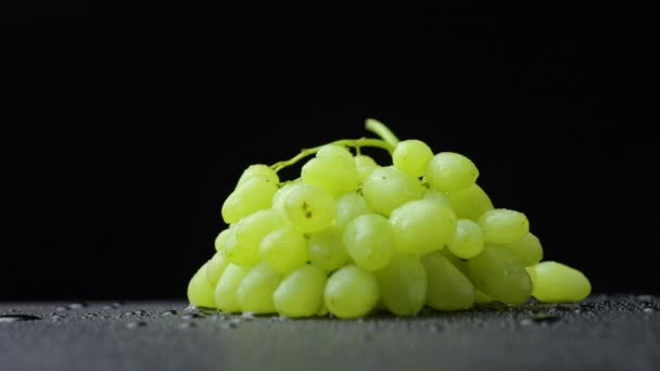 A bunch of ripe green grapes in drops of water rotates on a black studio background. Juicy sweet berries of grapes close up. Autumn harvest fruit screensaver. — Stock Video