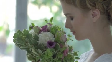 Young blonde girl in white vintage dress smeling flowers, cam moves upwards, slow motion