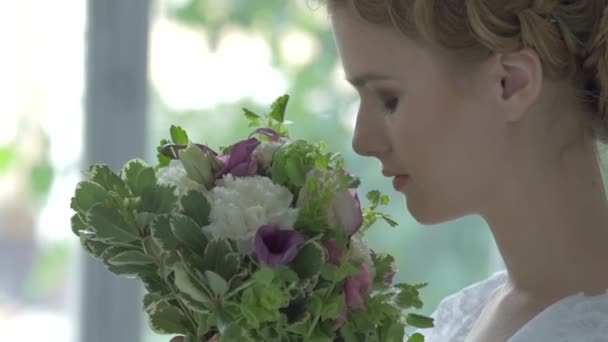 Young blonde girl in white vintage dress smeling flowers, cam moves upwards, slow motion — Stockvideo