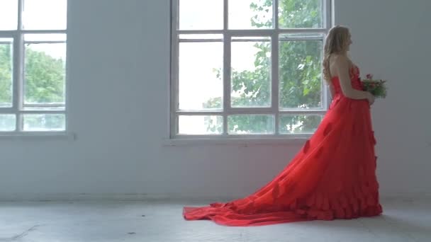 Belle fille en robe rouge magnifique continuer à marcher devant les fenêtres vintage avec des fleurs, au ralenti — Video