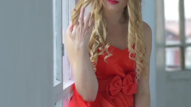 Beautiful young woman with wreath of red flowers on her head sitting on windowsill, smiling, cam moves upward, slow motion — Wideo stockowe