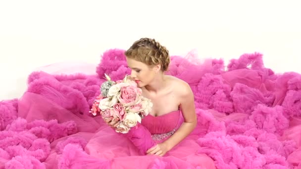 Bella giovane donna in splendido vestito rosa, seduta, annusa i fiori, sorridente, su bianco, rallentatore — Video Stock