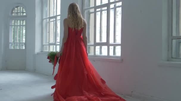 Hezká dívka v nádherné červené šaty, prochází kolem historických oken s květinami a její vlasy, zpomalené vlny
