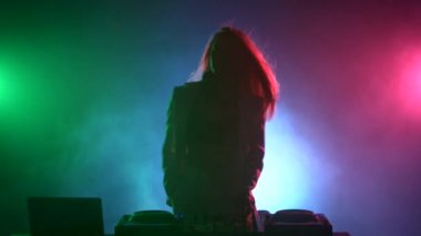 Güzel, gülümseyen, beyaz ceketli seksi dj kız, müzik çalan ve dans eden kulaklıklar, cepte el, duman, siluet