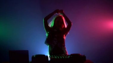 Seksi giysiler içinde Çekici dj kız, saç çevirme, eller yukarı, zevk, kulaklık, duman, arka ışık, siluet kullanarak