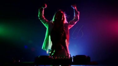 Young sexy, blonde woman dj, in white jacket and black top playing music using saxophone, flipping hair, dancing, hands up, claps, cam moves upwards, on green, pink and blue, backlight