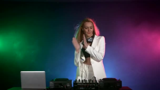 Schönes, lächelndes, sexy DJ-Mädchen in weißer Jacke, Kopfhörer, die Musik spielen und tanzen, Hand in der Tasche, klatscht, raucht — Stockvideo