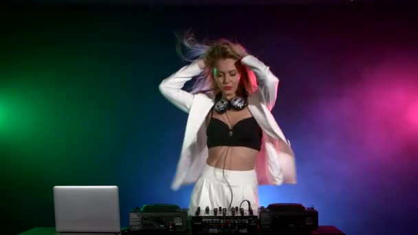 Hermosa, sonriente, sexy chica dj en chaqueta blanca, auriculares tocando música y bailando, humo — Vídeos de Stock