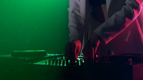 Hermosa, encantadora y sonriente chica dj con chaqueta blanca, auriculares en su oreja, tocando, escuchando música y bailando, humo, luz de fondo verde, mano en su bolsillo — Vídeo de stock