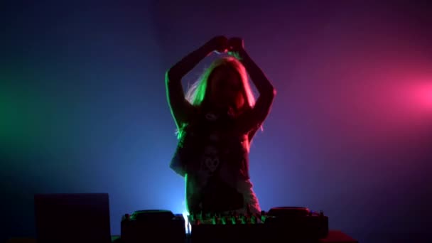 Atrakcyjna dziewczyna DJ w seksownych ubraniach, przerzucanie włosów, ręce w górę, cieszyć się nim, za pomocą słuchawek, dymu, podświetlenie, sylwetka — Wideo stockowe