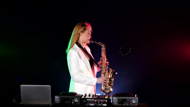 Young sexy, blonde woman dj in white jacket playing music using saxophone on black — 图库视频影像