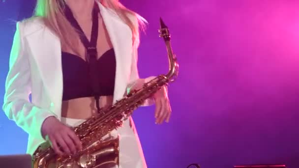 Young sexy, blonde woman dj in white jacket and black top playing music using saxophone, flipping hair, dancing, cam moves upwards — ストック動画