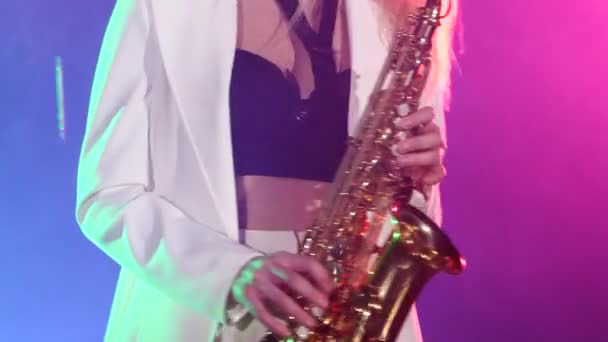 Young sexy, blonde woman dj in white jacket and black top playing music using saxophone, dancing, the camera shoots up to her waist — 图库视频影像