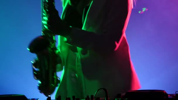 Jovem sexy, mulher loira dj em jaqueta branca e top preto tocando música usando saxofone, dançando, a câmera atira até a cintura, se move para cima, silhueta — Vídeo de Stock
