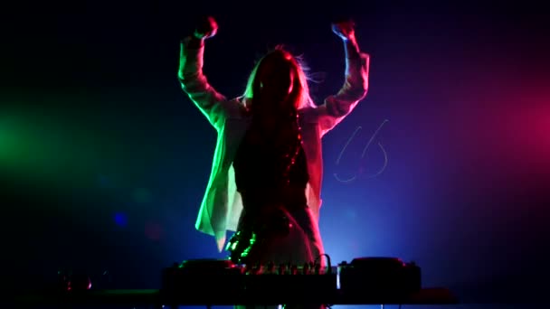 Young sexy, blonde woman dj, in white jacket and black top playing music using saxophone, flipping hair, dancing, hands up, claps, cam moves upwards, on green, pink and blue, backlight — Stockvideo