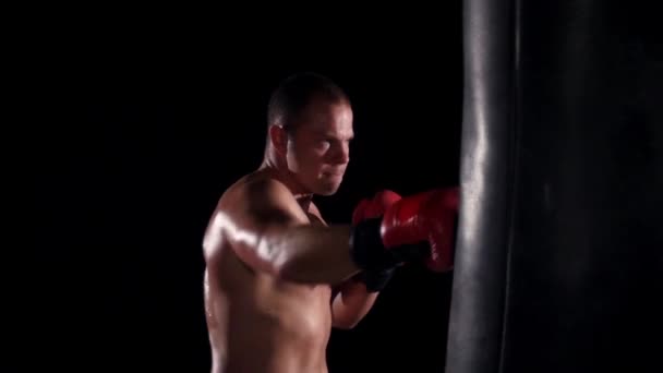 Boxeador hombre durante el boxeo golpeando bolsa pesada en el gimnasio de entrenamiento de fitness. Movimiento lento . — Vídeo de stock