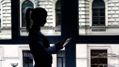 Öğle yemeği molasındaki kız tabletinde pencerede duran kitap okuyor. Siluet
