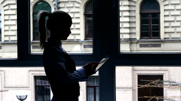 Meisje in de lunchpauze lezen boek op uw Tablet staande op het raam. Silhouet — Stockvideo