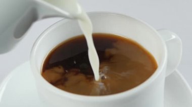 Taze süt kahve ile beyaz fincan içine dökülür, yavaş hareket, yakın