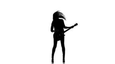 Beyaz bir arka plan üzerinde elektrik gitar çalan genç bir kızın silueti. Yavaş çekim.