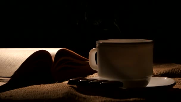Taza de café fresco con libro y barra de chocolate, sobre fondo negro — Vídeos de Stock