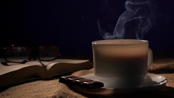 Csésze kávé kávéval csokoládé, poharak és nyitott könyv fekete háttérrel — Stock videók