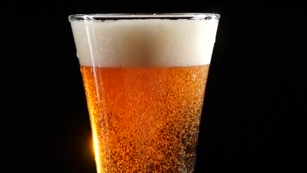 Bier ergießt sich in ein Glas auf schwarzem Hintergrund. Zeitlupe. — Stockvideo