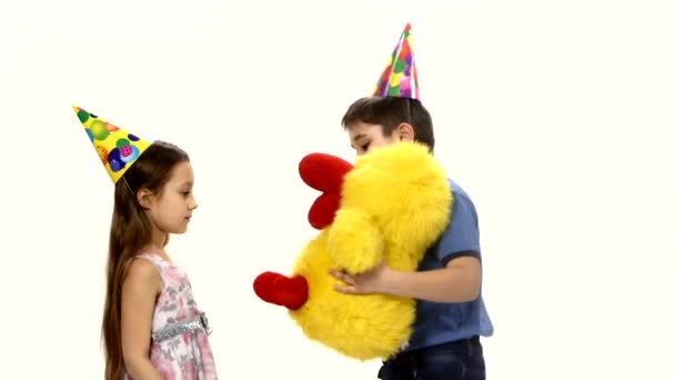 El niño le da a la niña un regalo de cumpleaños en forma de peluche de pollo amarillo — Vídeo de stock