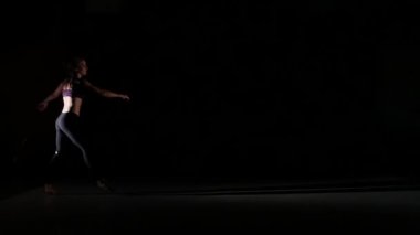 Sporty girl dancing contemp in the shadow on black background, slow motion