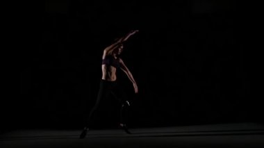 Young girl dancing contemp in the shadow on black background, slow motion