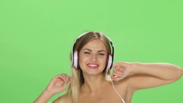 Joven hermosa chica rubia bailando con auriculares aislados en una pantalla verde — Vídeos de Stock