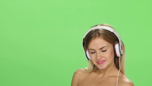 Fiatal gyönyörű szőke lány táncol fülhallgató elszigetelt zöld képernyőn — Stock videók
