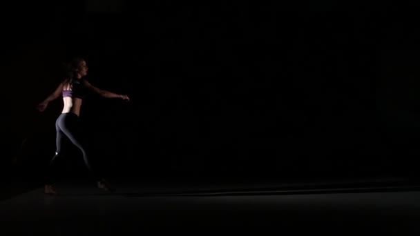 Спортивна дівчина танцює презирство в тіні на чорному тлі, повільний рух — стокове відео