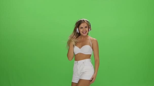 Joven hermosa chica rubia bailando con auriculares aislados en una pantalla verde — Vídeos de Stock