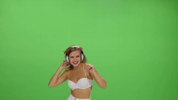 Joven hermosa chica rubia bailando con auriculares aislados en una pantalla verde — Vídeos de Stock