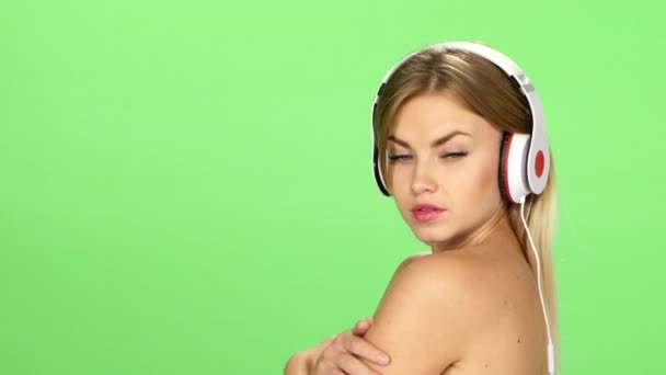 Joven chica rubia sexy bailando con auriculares aislados en una pantalla verde — Vídeo de stock