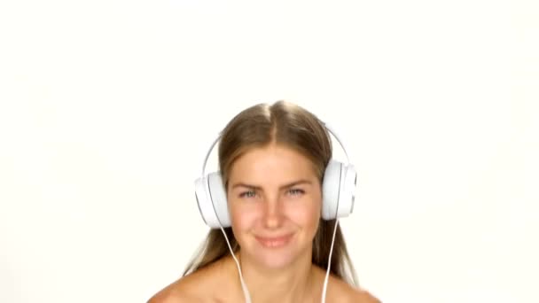 Mooie vrouw in hoofdtelefoon luisteren naar de muziek met fladderen op de wind haar over witte achtergrond — Stockvideo