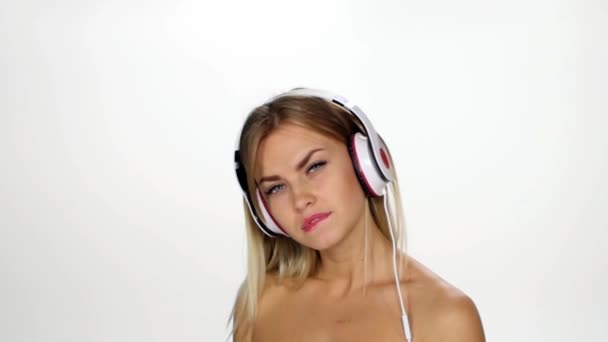 Mooie vrouwelijke in hoofdtelefoons luisteren naar de muziek met fladderen op de wind haar over witte achtergrond. Slow Motion. — Stockvideo