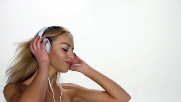 Schöne Frau mit Kopfhörern, die der Musik lauscht, mit flatternden Haaren auf weißem Hintergrund. Zeitlupe. — Stockvideo