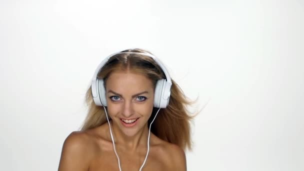 Bella femmina in cuffia ascoltando la musica con svolazzanti sui capelli del vento su sfondo bianco. Rallentatore . — Video Stock