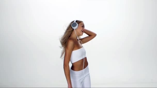 Красива жінка в навушниках слухає музику з мерехтінням на вітрове волосся на білому тлі. Повільний рух . — стокове відео