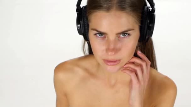 Όμορφο θηλυκό στα ακουστικά ακούγοντας τη μουσική με το φτερουγίσματα στα μαλλιά του ανέμου πάνω από το λευκό φόντο. Αργή κίνηση. — Αρχείο Βίντεο