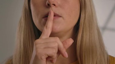 Uzun saçlı, parmağını dudaklarına dayayan, sessizliği ya da gizliliği simgeleyen bir kadının yakın plan fotoğrafı. Yavaş çekim.