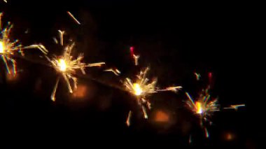 Kaleydoskop etkisi, parlak altın kıvılcımlar ve ince gökkuşağı parıltısıyla karanlık bir arka planda yanan kıvılcımlar. Tatiller, yeni yıl ve Noel için şenlik havası. Yavaş çekim.
