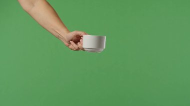 Yeşil krom arka planda beyaz kahve fincanı tutan bir kadın eli. Ofis, iş, eğitim, kafe veya kahve endüstrisiyle ilgili tasarımlar için çekilen.