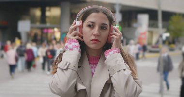 Kulaklık takan genç bir kadın hareketli bir caddede dururken müzik dinlemekten zevk alıyor..