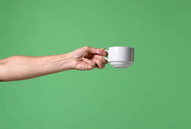 Yeşil krom arka planda beyaz kahve fincanı tutan bir kadın eli. Ofis, iş, eğitim, kafe veya kahve endüstrisiyle ilgili tasarımlar için çekilen.