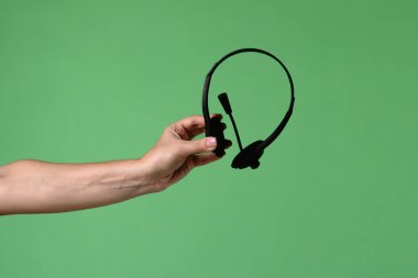 Yeşil renkli anahtar arka planında siyah kulaklık tutan bir kadın eli. Ofis işleri ve hizmet ve çağrı merkezi desteği ile ilgili bir tasarım için çekim.