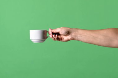 Yeşil krom arka planda beyaz kahve fincanı tutan bir kadın eli. Ofis, iş, eğitim, kafe veya kahve endüstrisiyle ilgili tasarımlar için çekilen.
