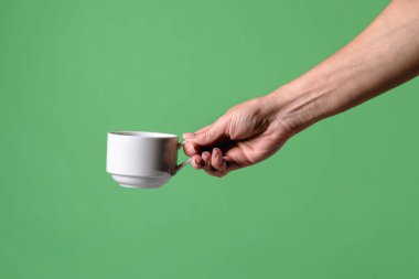 Yeşil krom arka planda beyaz kahve fincanı tutan bir kadın eli. Ofis, iş, eğitim, kafe veya kahve endüstrisiyle ilgili tasarımlar için çekilen.
